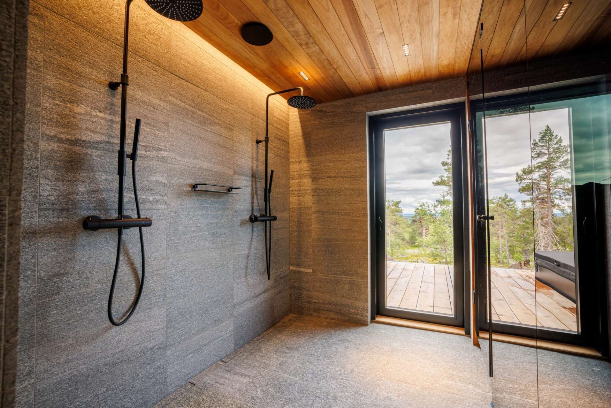 Ein modernes Badezimmer mit Steinwand, Holzboden und Glastür zu einer Terrasse mit Blick auf Bäume.