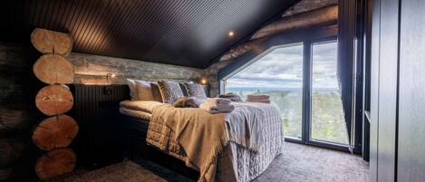 A bedroom with a large window, a bed with a blanket, and a wooden log wall.