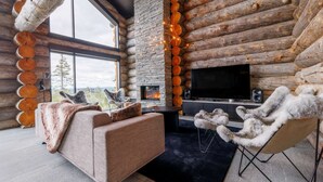A log cabin interior with a fireplace, a sofa, a chair, and a TV. - Luxury Villa Utsun Otso with breathtaking landscapes.  (Sirkka)