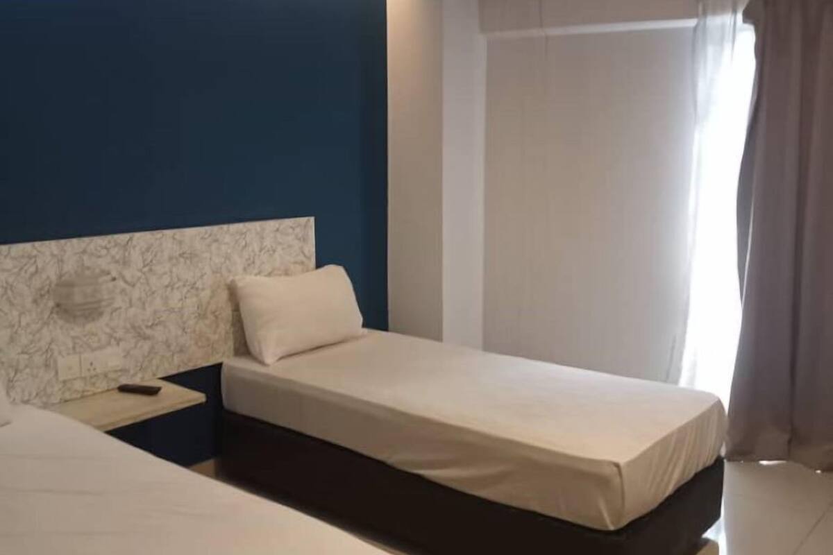 Ein Hotelzimmer mit zwei Einzelbetten, einem Marmorkopfstück, einem Nachttisch und einem Fenster mit Vorhängen.