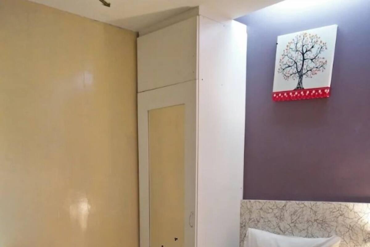 Ein Schlafzimmer mit einem Bett, einem Nachttisch, einer Tür und einem an der Wand befestigten Bild von einem Baum.