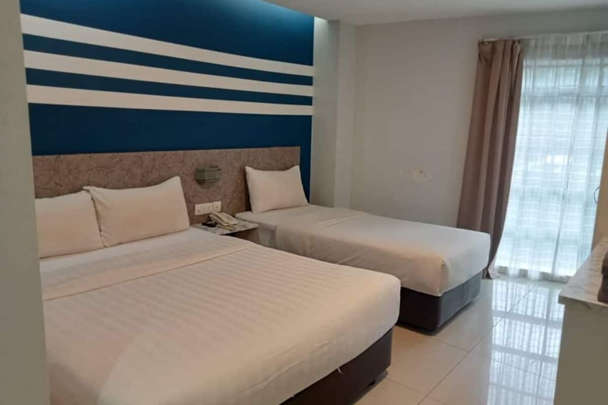 Ein Hotelzimmer mit zwei Betten, einem großen Fenster mit Vorhängen und einer Wandgestaltung in Blau-Weiß.