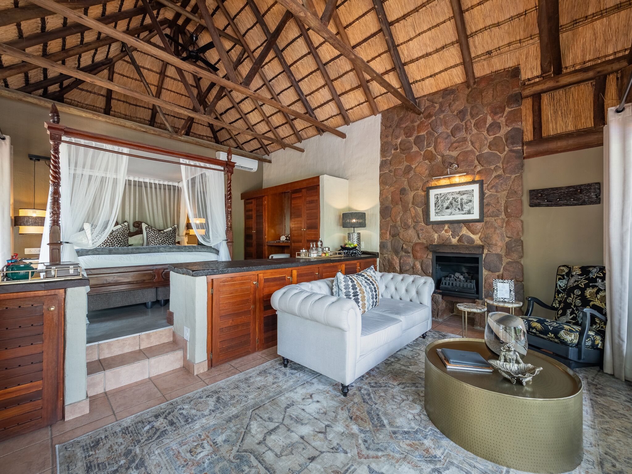 A spacious living area with a stone wall, a fireplace, a white sofa, and a wooden ceiling.