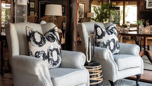 Une pièce spacieuse avec deux fauteuils, un tapis à motifs, un lustre et un plafond recouvert de chaume.