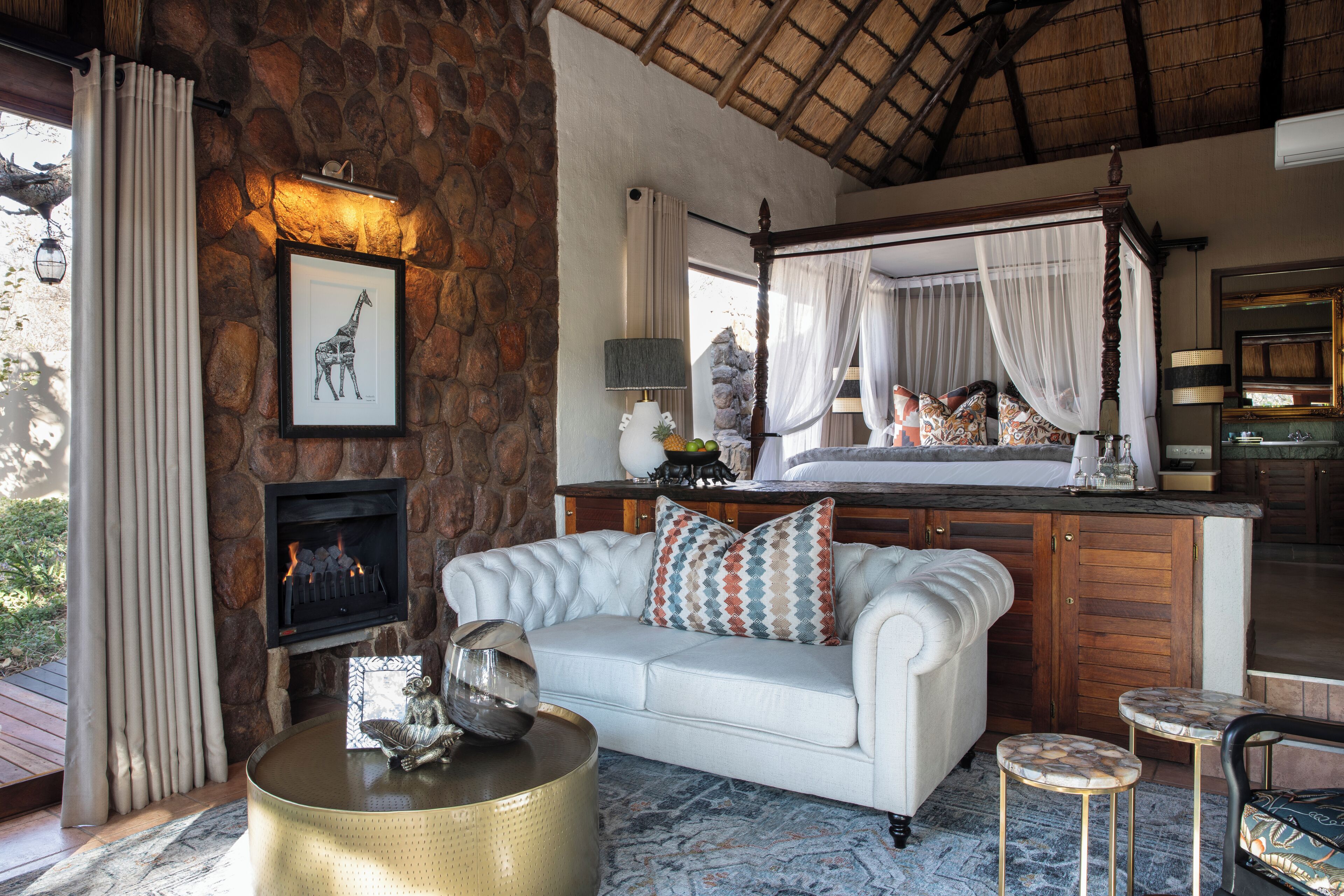 A cozy living area with a stone wall, a fireplace, a white sofa, a coffee table, and a four-poster bed.