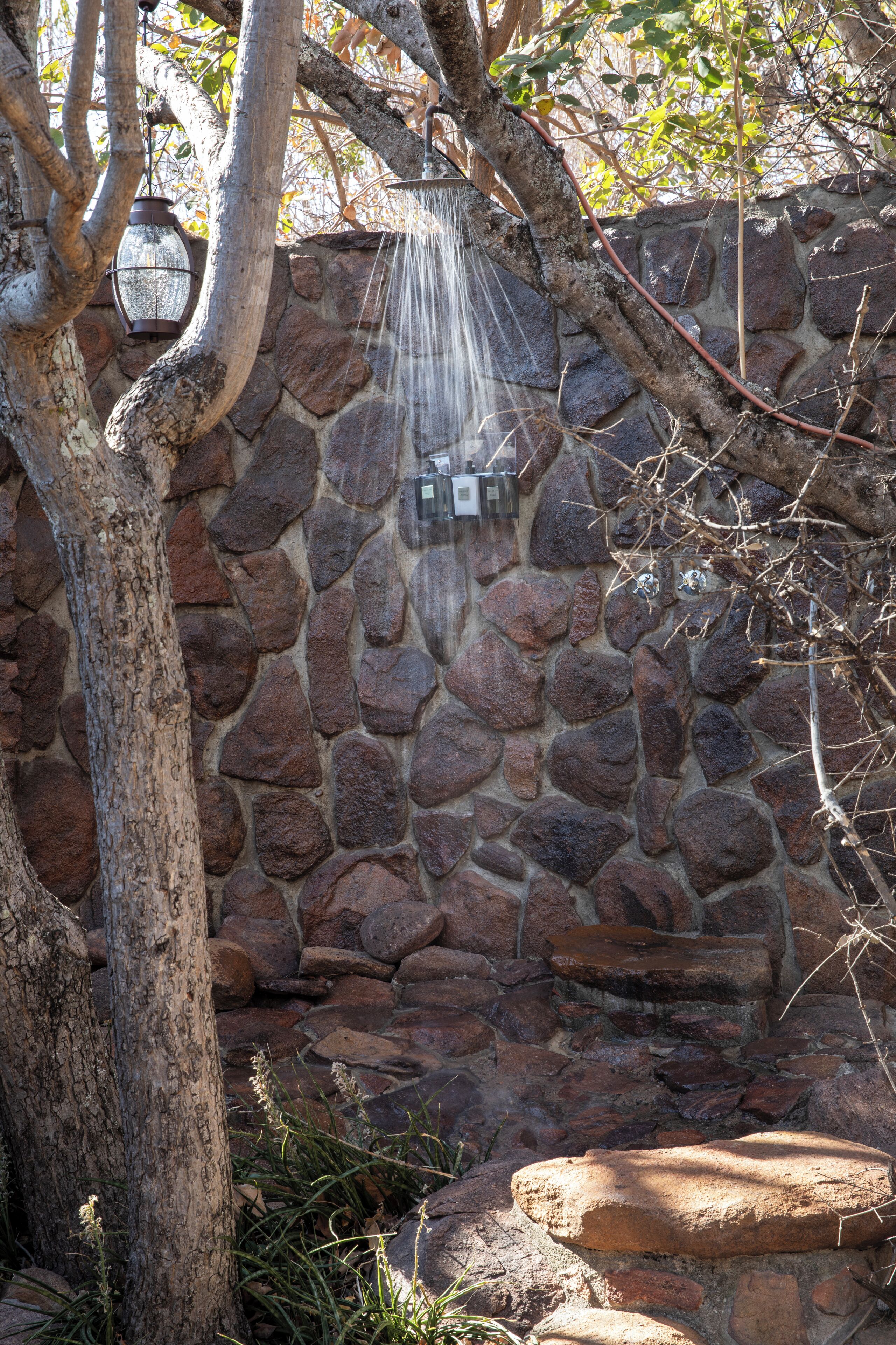 Un mur de pierre agrémenté d’un élément aquatique, comprenant une cascade et une lanterne suspendue.