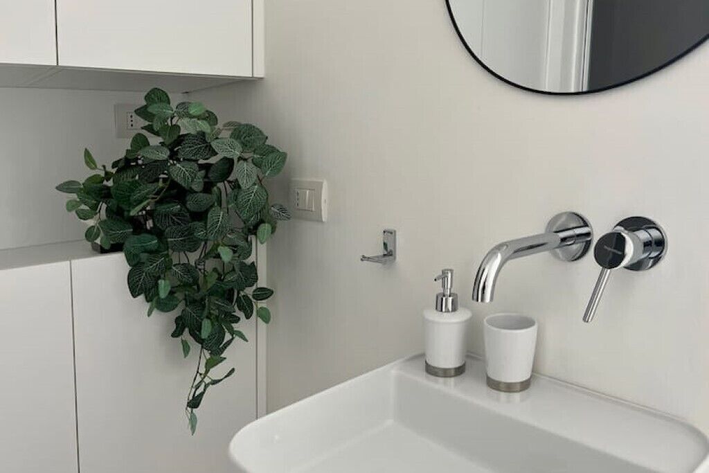A modern bathroom with a white sink, chrome faucet, and a potted plant.