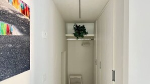 Un corridoio stretto con una porta bianca a destra, un piccolo tavolo bianco al centro e una pianta su uno scaffale sopra.