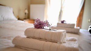 Ein ordentlich bezogenes Bett mit gefalteten Handtüchern und einer kleinen, violetten Blume darauf.