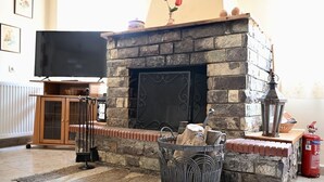 Ein Wohnzimmer mit Kamin aus Stein, einem Fernseher, einem Feuerlöscher und einem Korbkorb mit Holz.