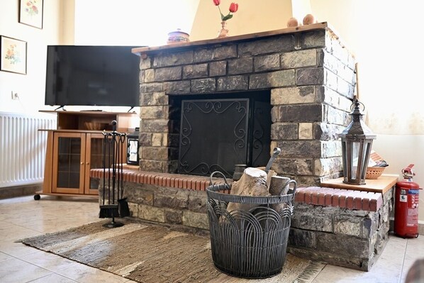 A living room with a stone fireplace, a television, a fire extinguisher, and a wicker basket with logs.