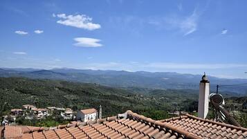 A terracotta-tiled roof, a white building with a bell tower, and a mountainous landscape in the background.
