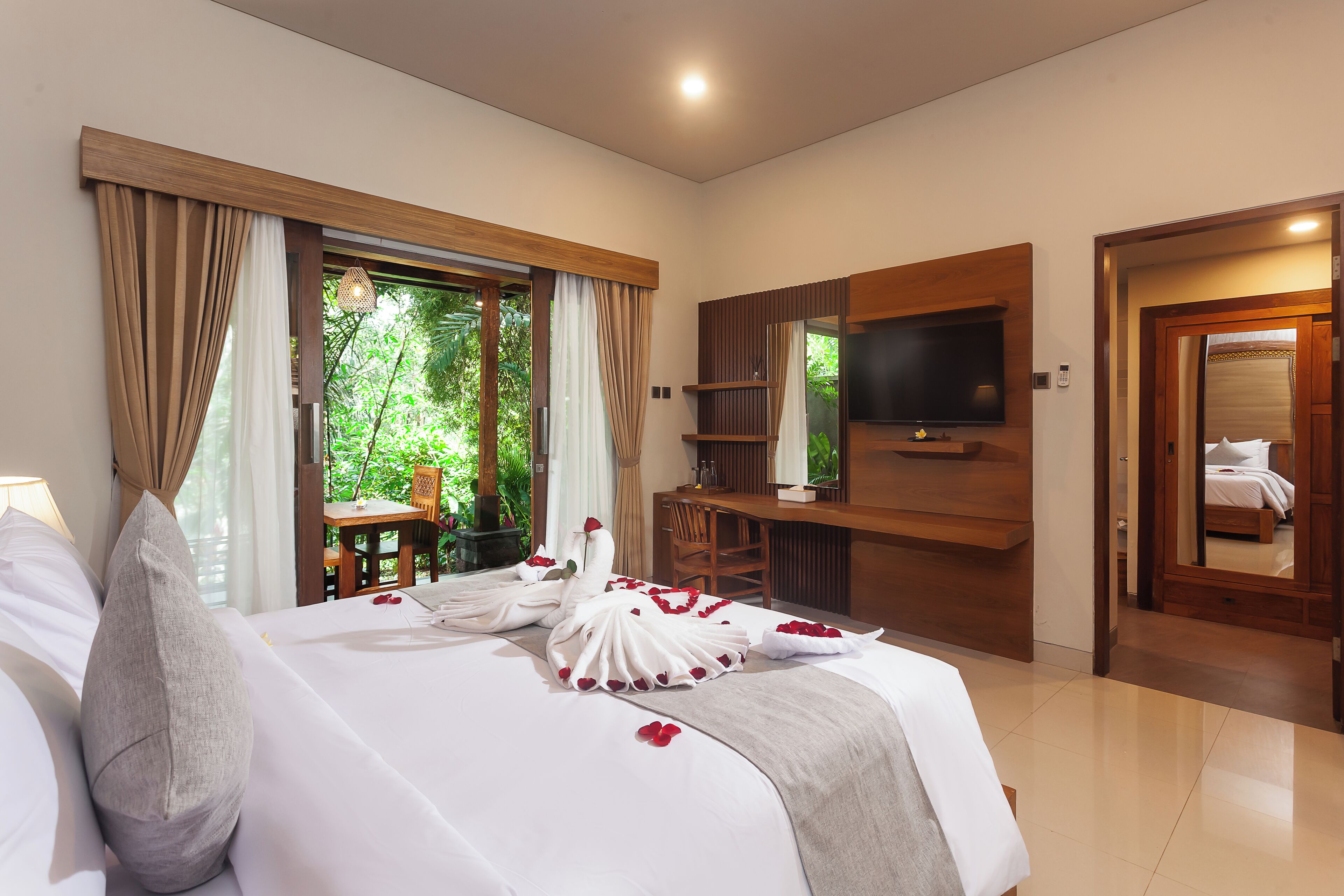 A hotel room with a bed, a desk, a TV, and a view of greenery.
