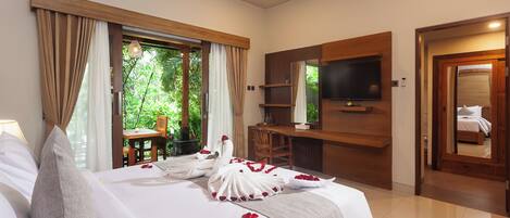 A hotel room with a bed, a desk, a TV, and a view of greenery.