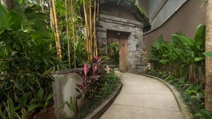 Un sendero bordeado por abundante vegetación y estatuas de piedra, que conduce a un edificio con entrada curva.