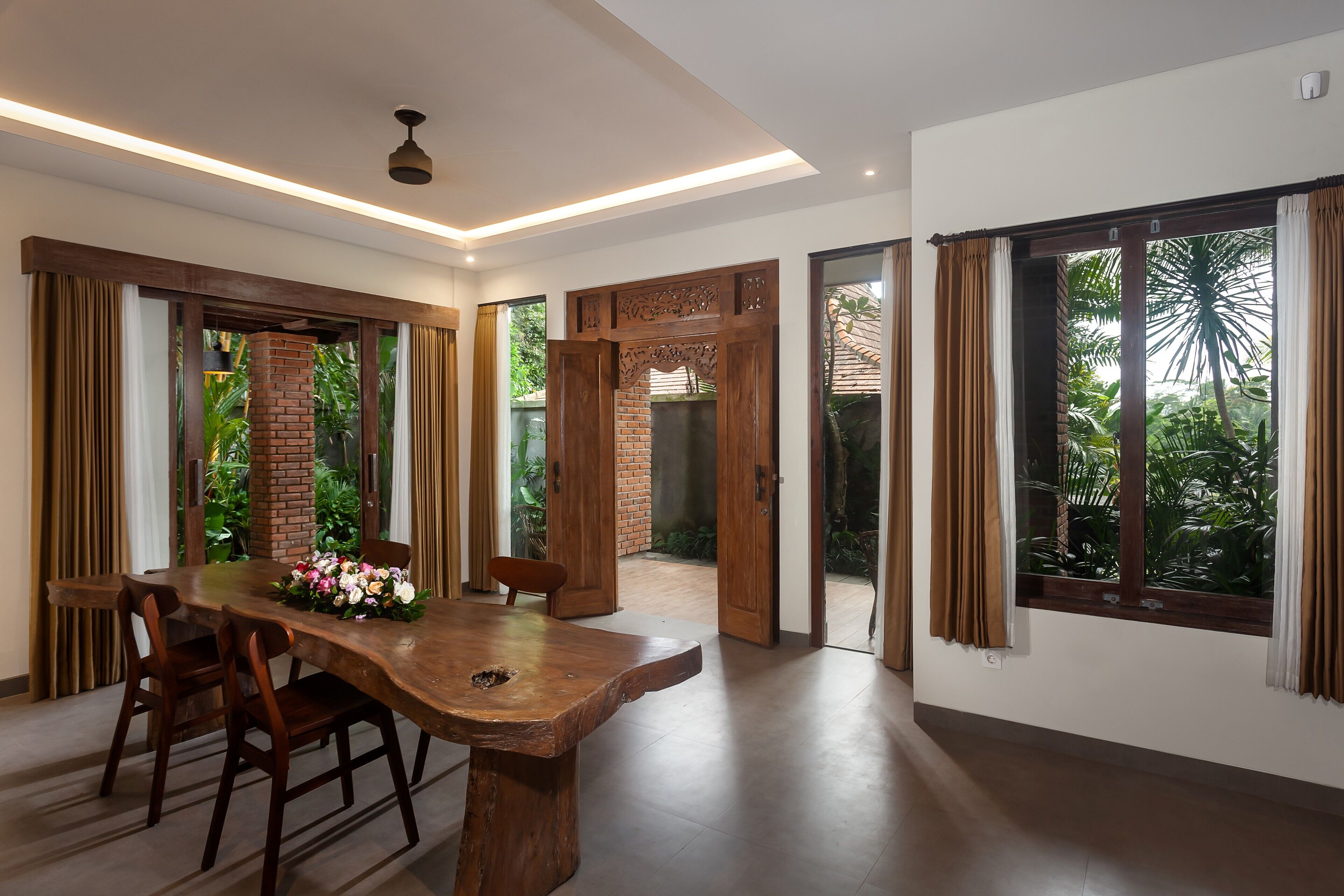 Un comedor amplio con mesa y sillas de madera, ventanas grandes con cortinas y vista a zonas verdes.