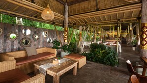 Un espacio de descanso al aire libre con techo, muebles de mimbre, una mesa de madera y luces colgantes.