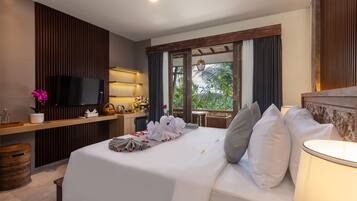 A hotel room with a bed, a TV, a desk with a lamp, and a view of greenery outside.