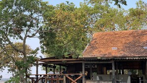 A rustic wooden building with a tiled roof, a wooden deck, and a large wheel structure.