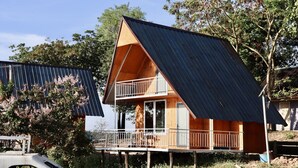 A two-story wooden cabin with a sloped metal roof, a balcony, and a wooden deck.