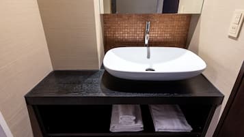 A bathroom with a white sink, black countertop, and a mirror above it. There are two towels in a drawer below the sink.