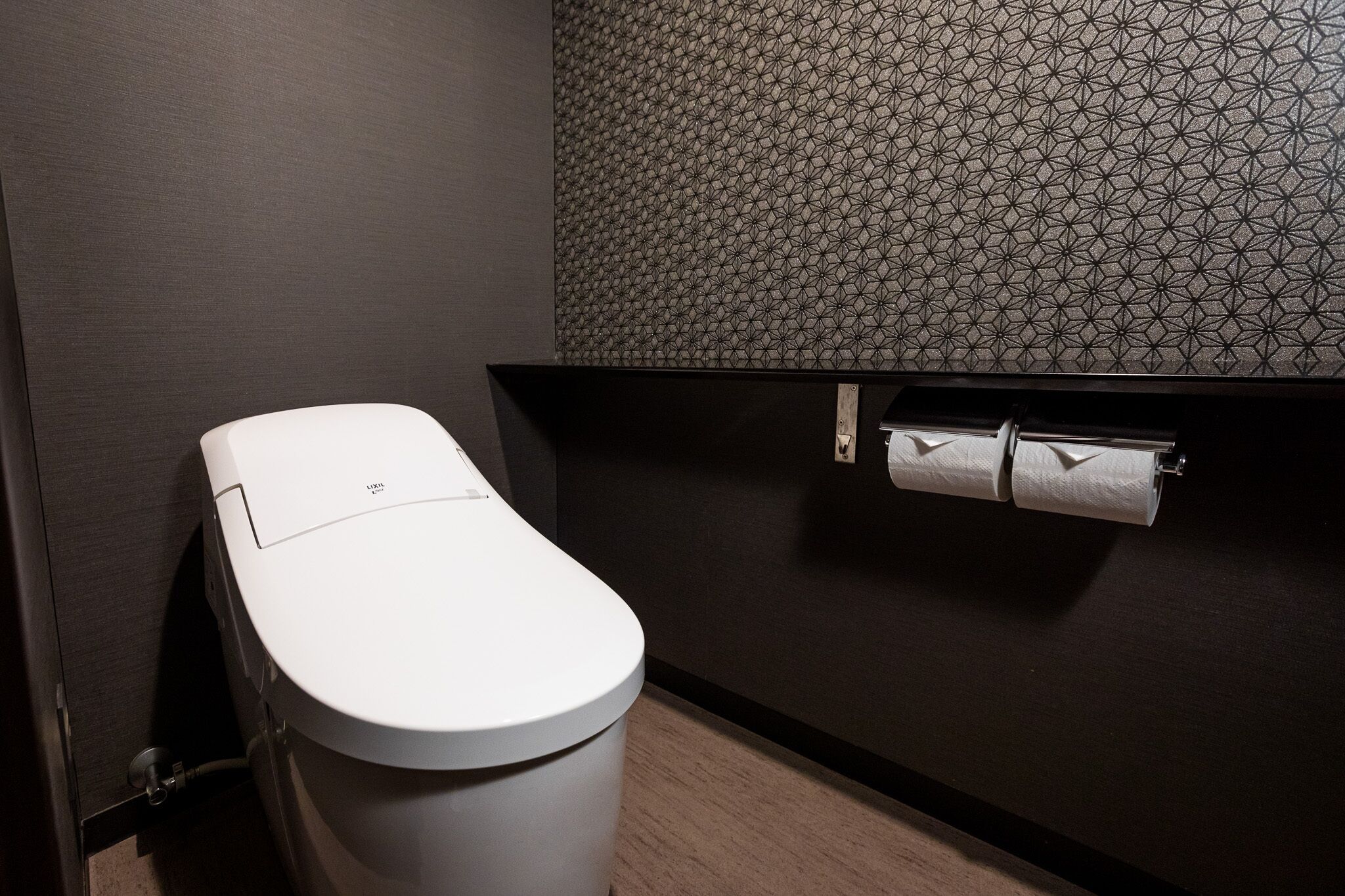 Un baño moderno con inodoro, pared con diseño y dispensador de papel higiénico.