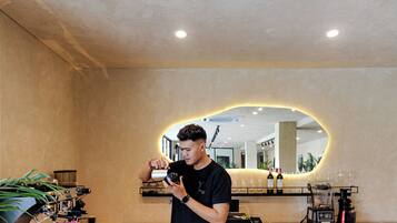 A person preparing a drink at a bar with a coffee machine and wine bottles in the background.