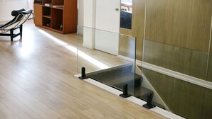 Una habitación con piso de madera, una silla negra, un panel de vidrio y una puerta blanca.