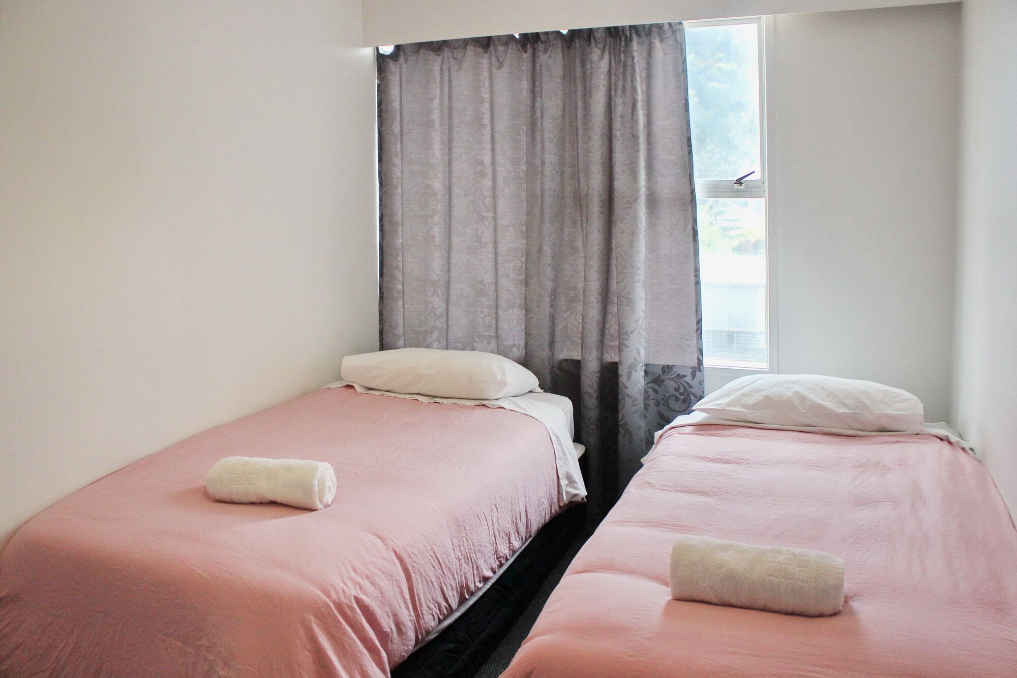A room with two single beds, each with a pillow and a rolled towel.