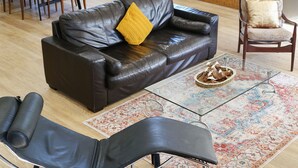Una sala de estar con un sofá de cuero oscuro, una mesa de centro de vidrio, una alfombra estampada y un sillón de cuero negro.