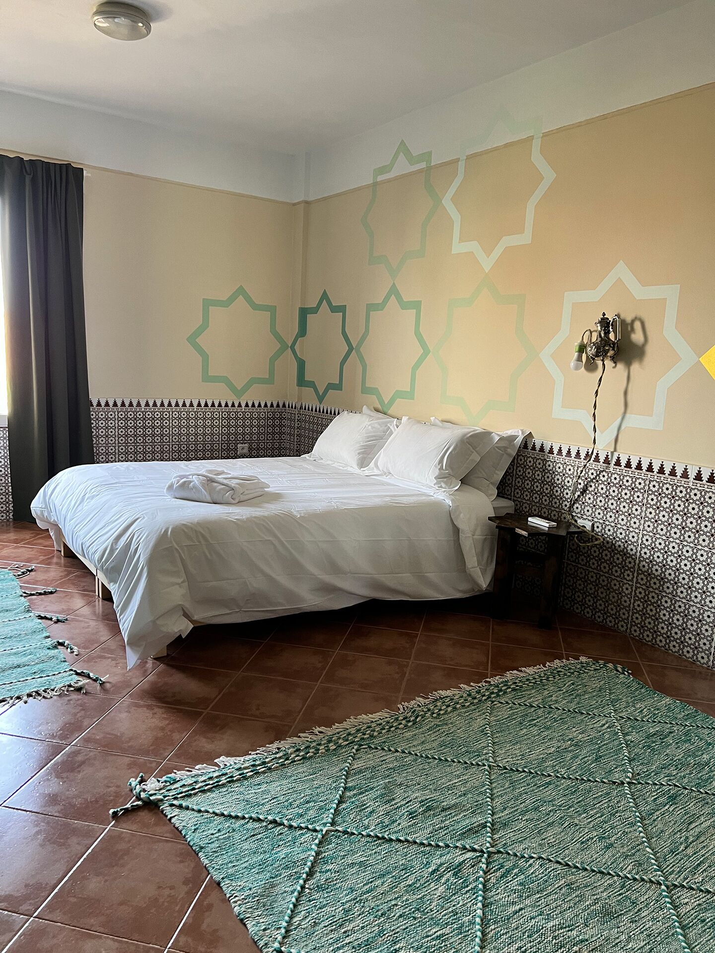 A neatly made bed with white linens, a patterned rug, and a wall with geometric designs.