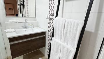 Un baño moderno con un lavamanos blanco, tocador de madera oscura, un perchero negro y azulejos con diseño.
