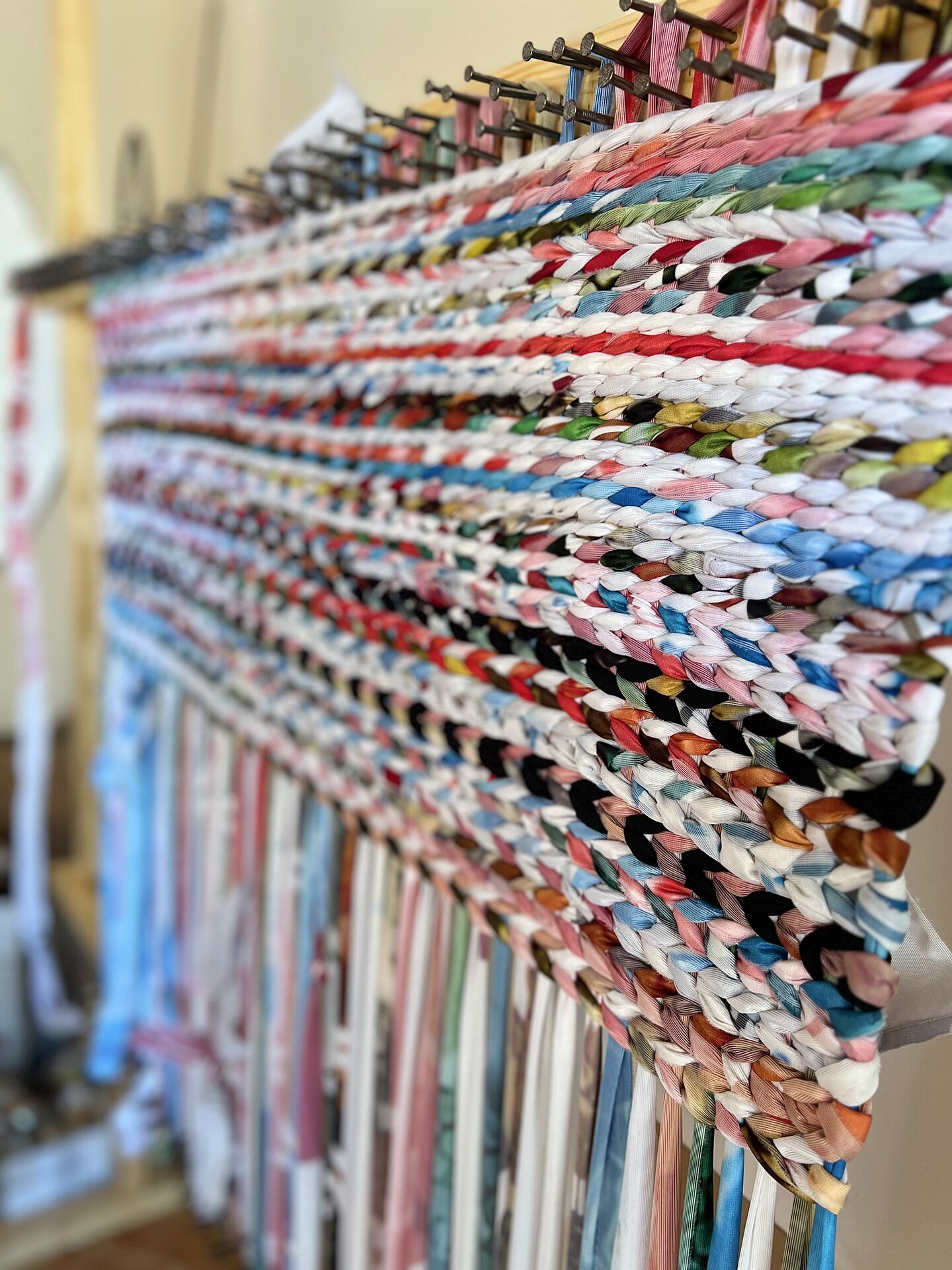 Eine Wand mit bunten, gewebten Textilien, die auf einem Gestell präsentiert werden.