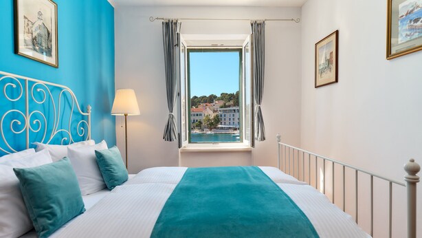 Hotellihuone, jossa on sänky, ikkuna verhoilla, lamppu ja näkymä kaupunkiin.