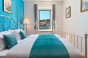 A hotel room with a bed, a window with curtains, a lamp, and a view of a town. - Sun Spalato Fara (Hvar)
