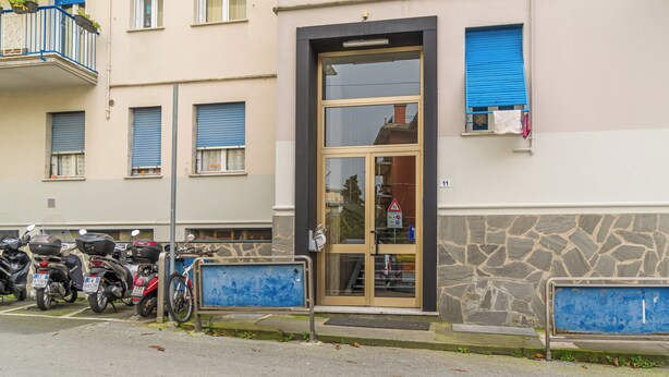 Un edificio con fachada de piedra, puerta de entrada de vidrio y una ventana con persianas azules.