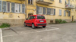 Un coche rojo aparcado en un espacio de estacionamiento delimitado frente a un edificio amarillo con varias ventanas y contraventanas.