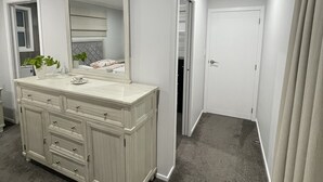 A bathroom with a vanity, a mirror, a clock, and a door leading to another room. - Private Ensuite with Hot Spa at Upper Hutt, Wellington (Upper Hutt)