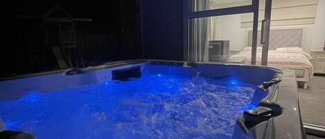 A hot tub with a blue light, a bed, and a window in the background.