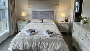 A neatly arranged bedroom with a large bed, two bedside tables with lamps, a dresser, and a window with curtains. - Private Ensuite with Hot Spa at Upper Hutt, Wellington (Upper Hutt)