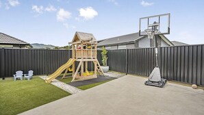 A backyard with a wooden playhouse, a basketball hoop, and a lawnmower. - Private Ensuite with Hot Spa at Upper Hutt, Wellington (Upper Hutt)