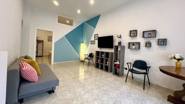 A modern living room with a grey sofa, a TV, and a blue accent wall. - B&b Margherita Torremaggiore (Torremaggiore)
