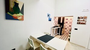 A small, well-lit room with a white table and chairs, a painting on the wall, and a door leading to another room. - B&b Margherita Torremaggiore (Torremaggiore)