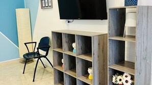 A modern room with a large flat-screen TV mounted on the wall, wooden shelving units, a blue chair, and a vase with flowers. - B&b Margherita Torremaggiore (Torremaggiore)