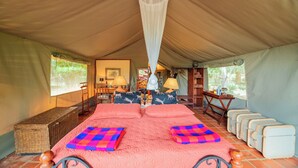 A tented room with a bed, pillows, a hanging mosquito net, a table with lamps, and a bench. - Buffalo's Rest  (Naivasha)