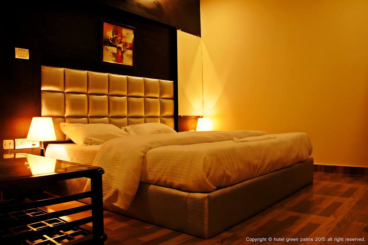 A hotel room with a large bed, two bedside lamps, a wooden nightstand, and a headboard with a tufted design.