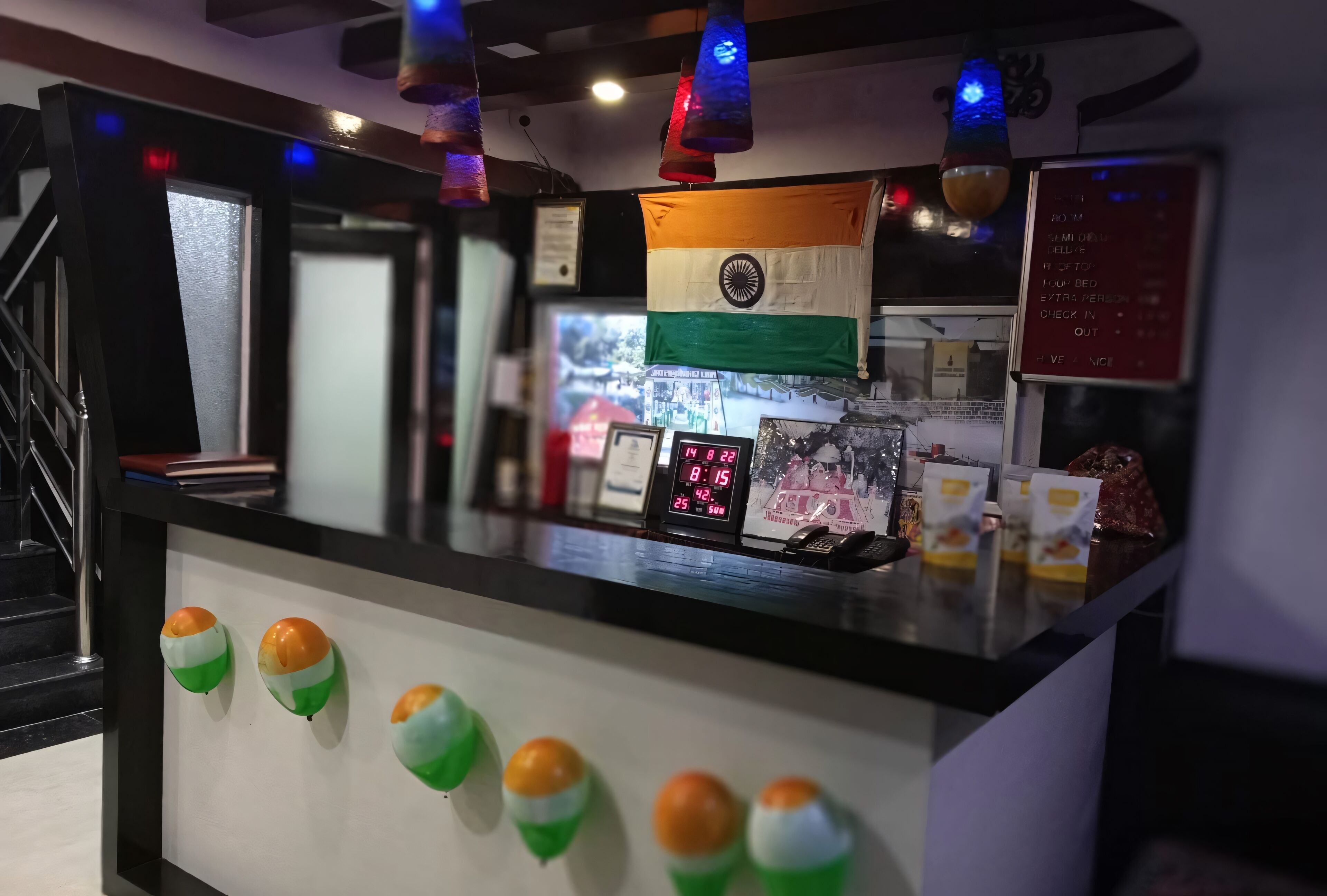 A reception desk with an Indian flag, a digital clock, and a menu board.