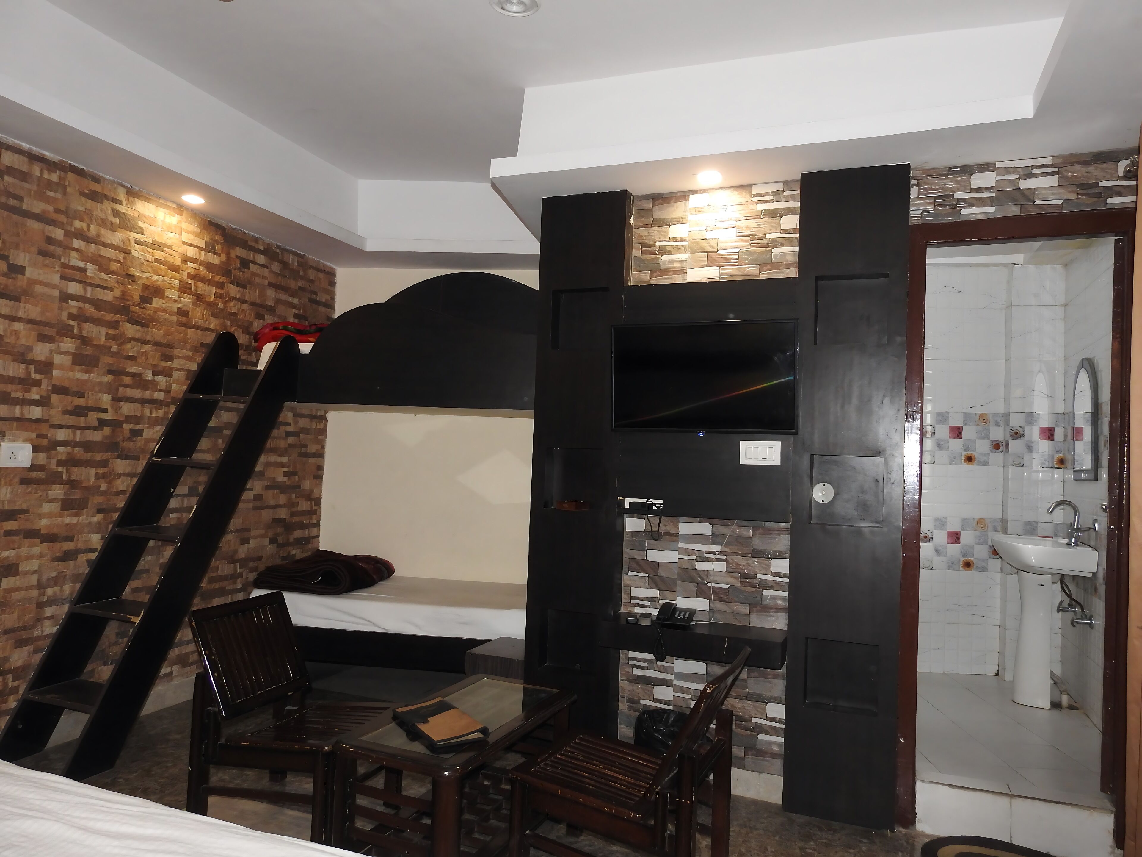 Une chambre avec un lit superposé, un bureau avec une chaise, une échelle, une télévision et une salle de bain avec des toilettes et un lavabo.