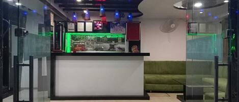 Un área de recepción con mostrador, sofá verde y ventilador.