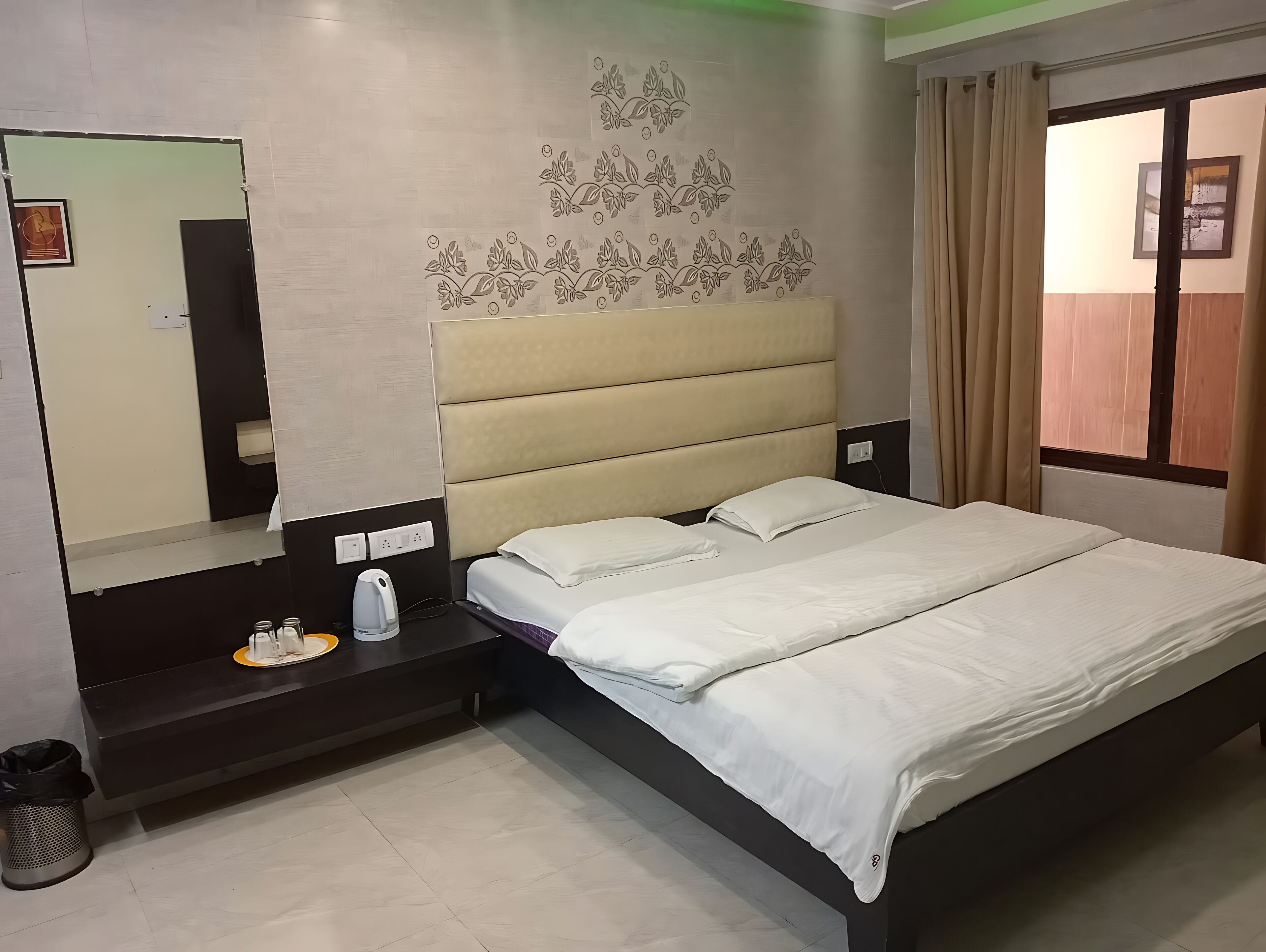 A hotel room with a bed, a nightstand, a mirror, and a window with curtains.